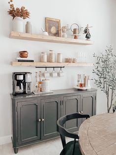 there is a coffee maker on the shelf above the counter in this kitchen with gray cabinets and black chairs