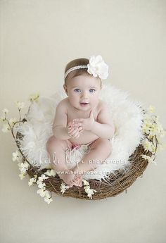 a baby is sitting in a nest with flowers on it's head and smiling at the camera