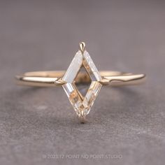 a yellow gold ring with an irregular cut diamond in the center, sitting on a gray surface