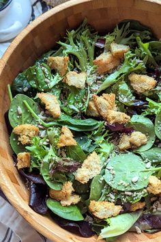 a wooden bowl filled with green salad and croutons