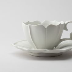 a white tea cup and saucer on a white tablecloth with the shape of a flower