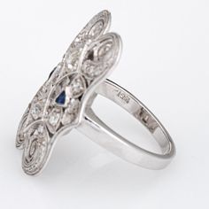 Finely detailed vintage Art Deco era diamond & sapphire ring (circa 1920s to 1930s) crafted in 14k white gold.   Two old mine cut diamonds are estimated at 0.10 carats each, accented with a further 8 estimated 0.02 carat diamonds. The total diamond weight is estimated at 0.36 carats (estimated at I-J colour and SI1-2 clarity). Two French cut sapphire total an estimated 0.06 carats.   The finely detailed Art Deco era ring features scrolled filigree with mil grain overlay details in an elongated d Art Deco Sapphire Ring With Diamond Accents, Elegant Sapphire Ring With Intricate Diamond Design, Elegant Sapphire Ring With Intricate Design For Anniversary, Classic Sapphire Ring With Intricate Design For Anniversary, Formal Victorian Sapphire Ring Accented With Diamonds, Victorian Sapphire Ring With Diamond For Formal Occasions, Victorian Sapphire Ring With Diamond Cut For Anniversary, Antique Silver Diamond Ring With Sapphire, Antique Silver Sapphire Diamond Ring