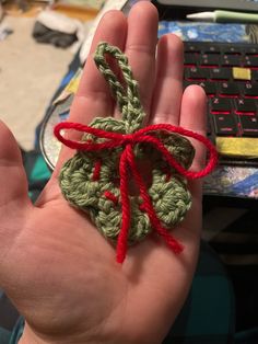 a hand holding a small crocheted object with red string on it's thumb