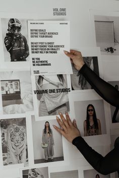 a woman in black shirt pointing at pictures on wall with white lettering and images behind her