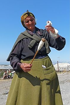 an old woman is holding a bird in her hand and wearing a green skirt with pockets