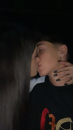 a woman with black nails kissing a man in the dark