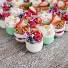 desserts are arranged in small cups on a wooden table with strawberries, raspberries and other toppings