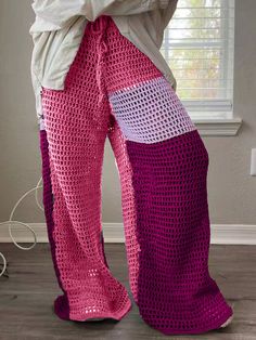 a woman standing in front of a window wearing pink and white crocheted pants