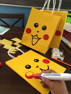 a person is drawing on some yellow paper bags with red noses and eyes, while another hand holds a marker