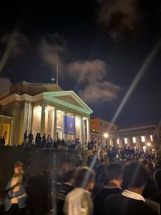 a crowd of people standing in front of a building at night with lights shining on it