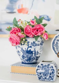 pink roses are in a blue and white vase on a shelf next to two books