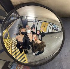 three women taking a selfie in a mirror at the subway station with their hands up