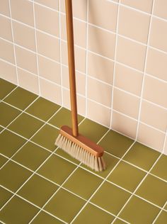 a broom is sitting on the floor in front of a tiled wall with brown and white tiles