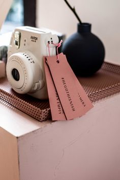 a white camera sitting on top of a table next to a black vase and tag