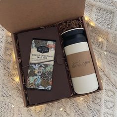 a coffee cup and book in a gift box with lights on the floor next to it