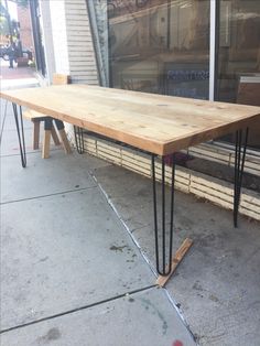 a wooden table sitting on top of a sidewalk next to a store front window with black hairpin legs