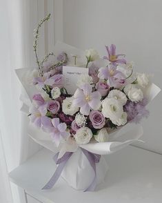 a bouquet of white and purple flowers with a card in the middle on a table