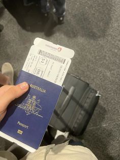 a person holding a blue australian passport in their hand and luggage behind them on the floor