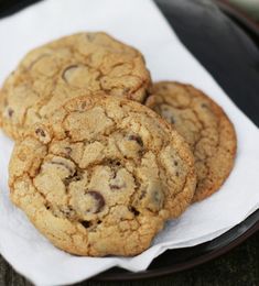 three chocolate chip cookies sitting on top of a white paper towel in a black plate