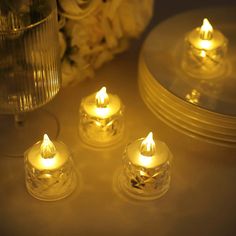 three lit candles sitting on top of a table next to some plates and vases