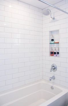 a bathroom with white tile walls and a bathtub in the corner, along with shelves on the wall