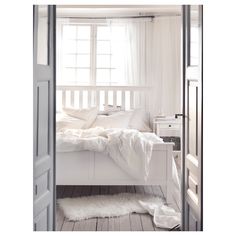 a white bed sitting in a bedroom next to an open door with curtains on it