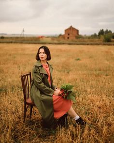 a woman sitting on a chair in the middle of a field with an old building in the background