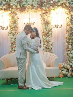 a newly married couple standing in front of a floral arch with flowers on the wall