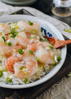 shrimp and rice with peas in a white bowl on a wooden tray next to silverware