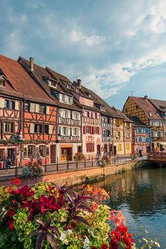 colorful buildings line the side of a river in europe, with people walking along it