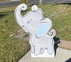 an elephant cut out sitting in the grass next to a sidewalk and street with cars on it