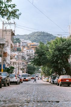 a man walking down the middle of a cobblestone street with cars parked on both sides