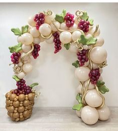 an arch made out of balloons with grapes and leaves on the top, next to a basket of grapes