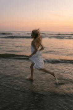 a blurry photo of a woman running on the beach at sunset with her hair blowing in the wind