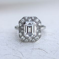 an emerald cut diamond surrounded by pave set diamonds on a white surface with intricate details