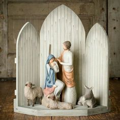 a figurine of jesus and two sheeps in front of a wooden fence