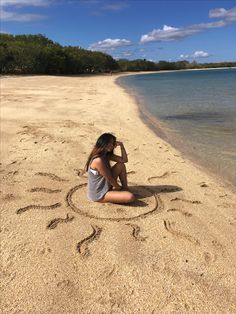 a woman sitting on top of a sandy beach next to the ocean and writing in the sand