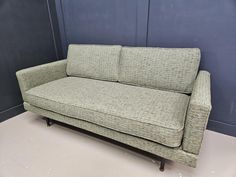 a green couch sitting on top of a hard wood floor next to a blue wall