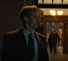 a man wearing a suit and tie standing in front of a doorway with other people