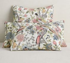 two pillows with birds and flowers on them sitting next to each other in front of a white wall