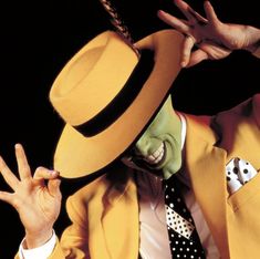 a man in a yellow suit and hat making the peace sign with his hands while wearing a polka dot tie