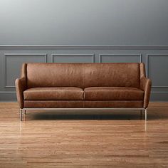 a brown leather couch sitting on top of a hard wood floor next to a lamp