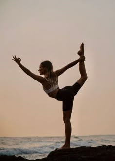 a woman is doing yoga on the rocks by the ocean at sunset or dawn, with her arms stretched out