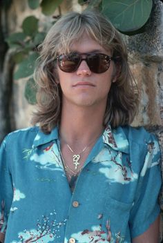 a man wearing sunglasses standing next to a tree