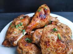 some chicken legs are on a white plate with parsley sprinkled around them