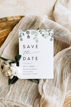 an elegant save the date card with greenery and flowers sits on top of a blanket