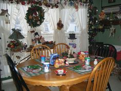 a dining room table and chairs with plates on it, christmas wreaths hanging from the window