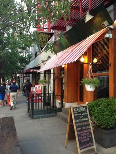 people walking down the sidewalk in front of a restaurant with awnings over it