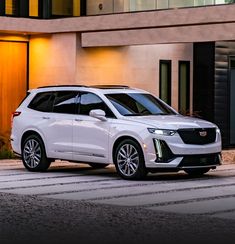 a white cadillac suv parked in front of a building at night with its lights on