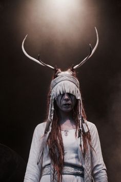 a woman with long hair and horns on her head standing in front of a spotlight